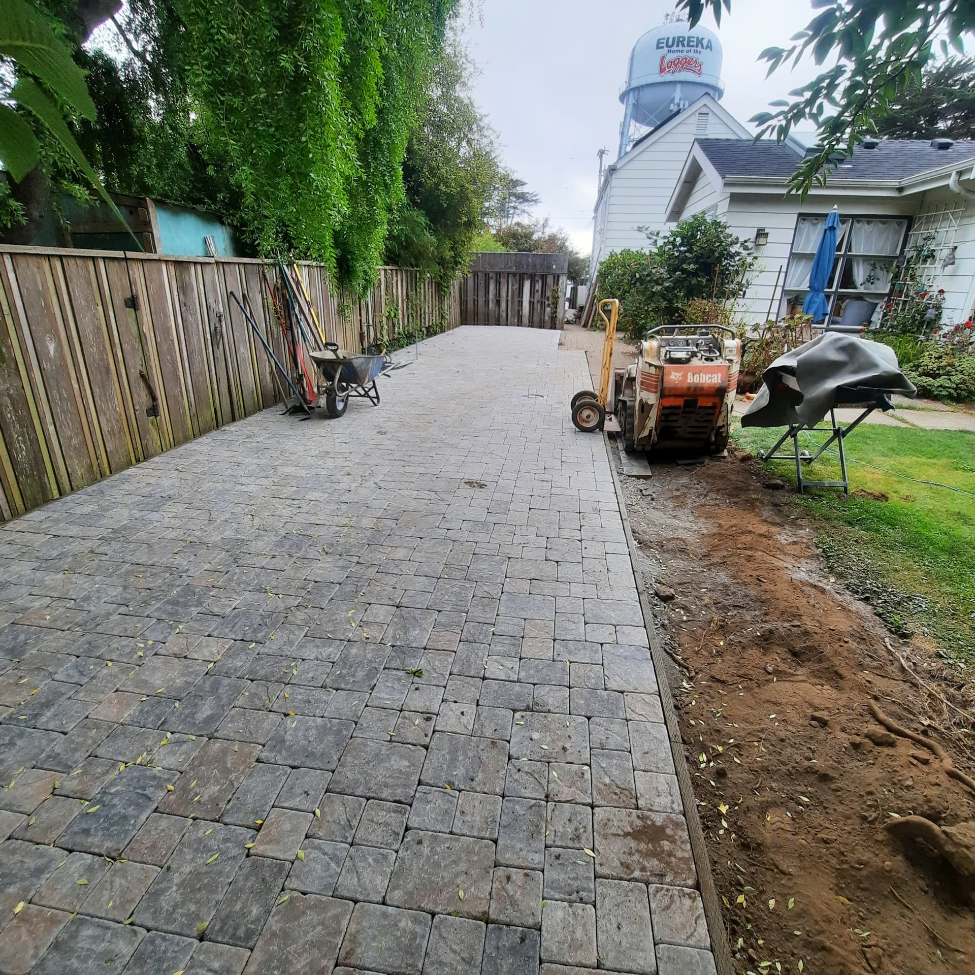 A compact mini skid steer working alongside a paver driveway in a fenced residential backyard in Eureka.
