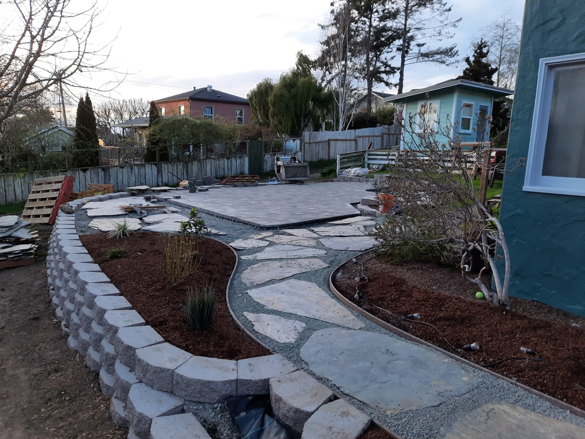 Backyard renovation with a large paver patio, flagstone paths, and a curved mulched planting bed