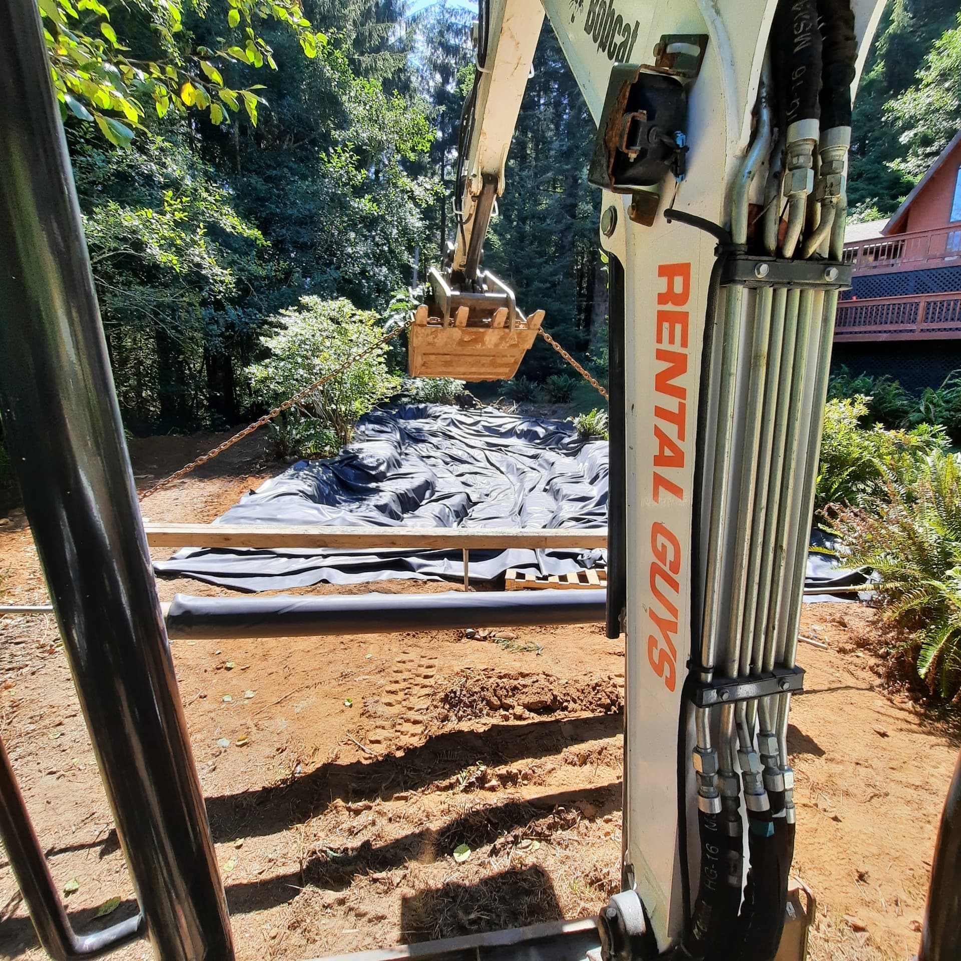 An excavator bucket lowering a pond liner into an excavated basin on a Humboldt County property.