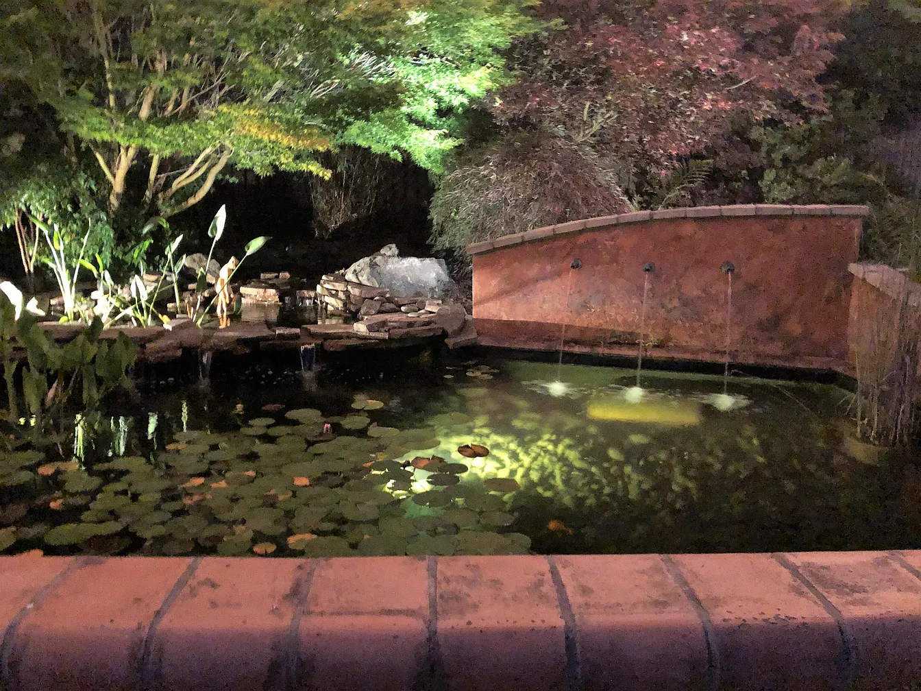 Pond and waterfall at night, lit with warm low-voltage landscape lighting.