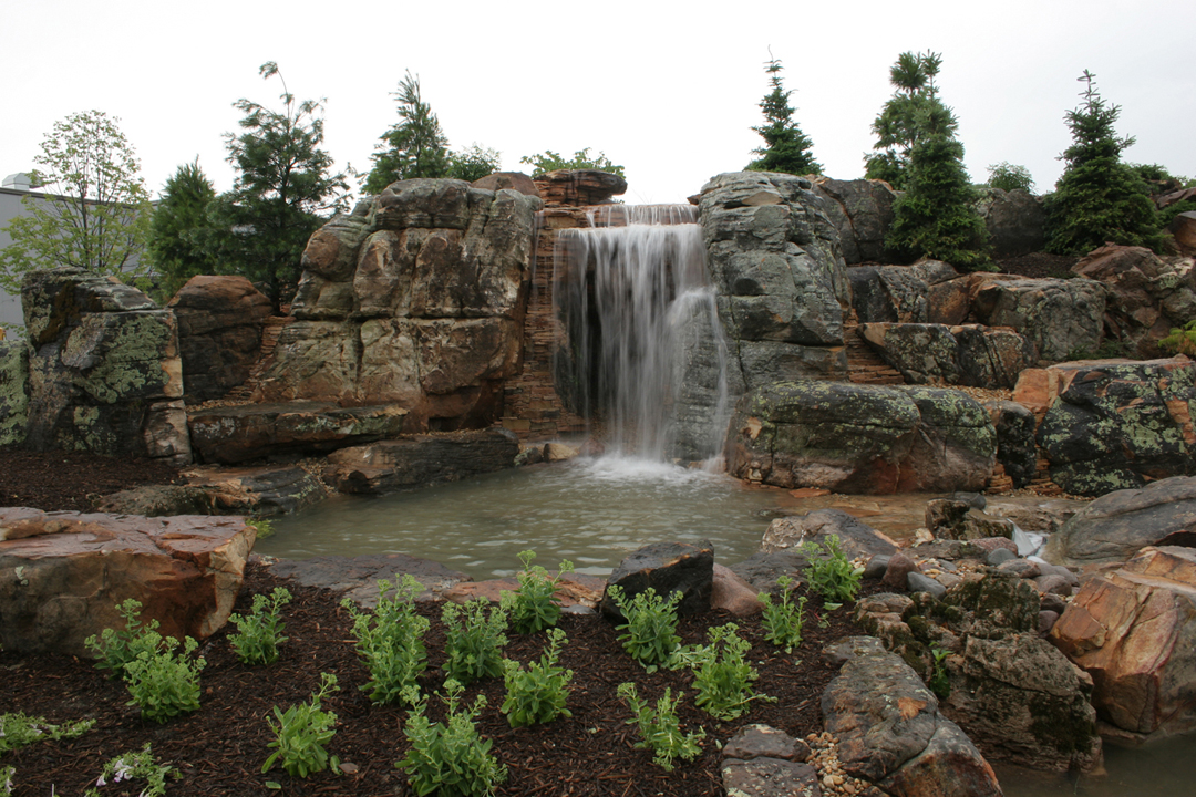 Completed main waterfall of Aquascape's large constructed water feature, with stacked stone ledges, a wide falls and a planted pool below.
