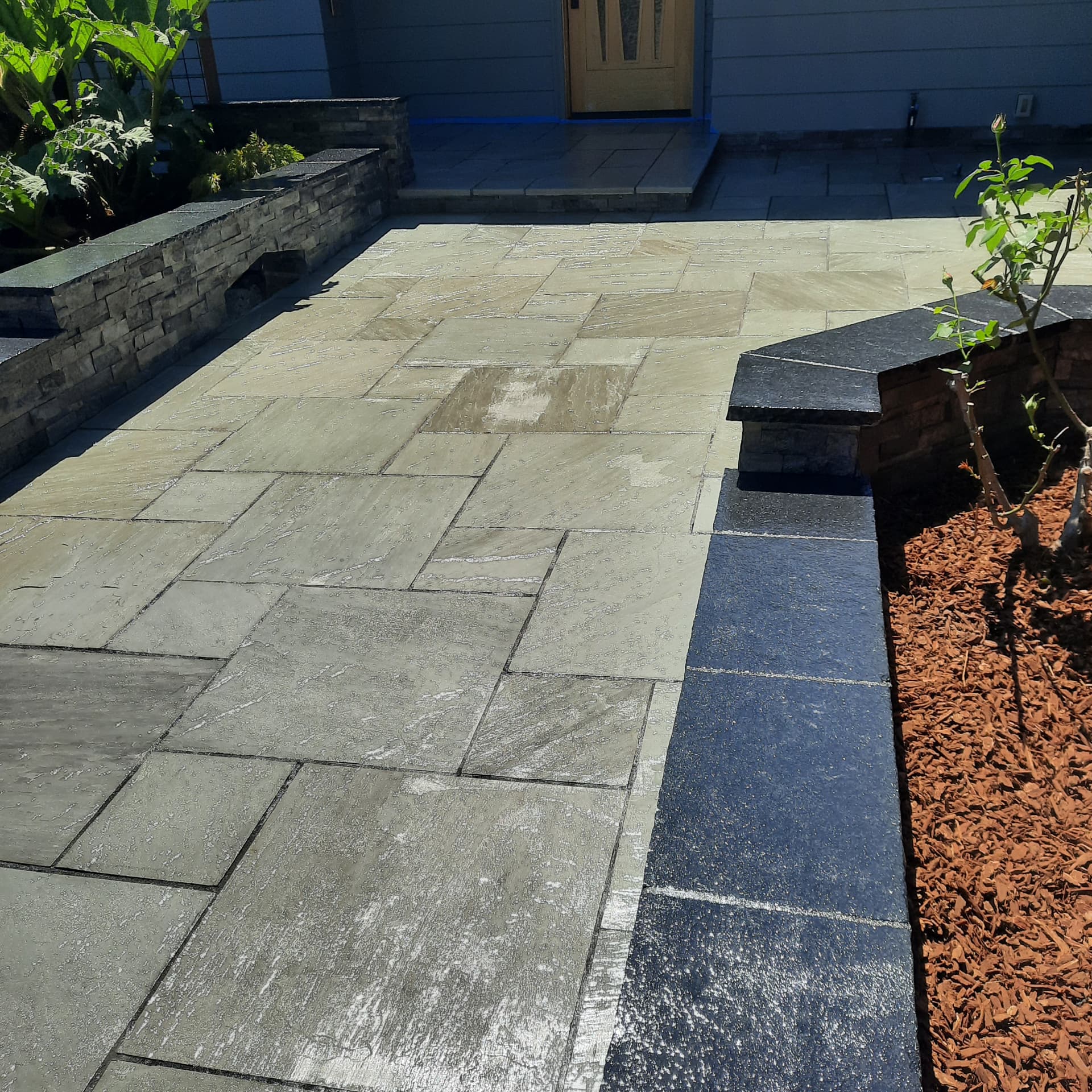 Finished large-format stone paving at the main approach with dark-capped masonry walls leading to the front door