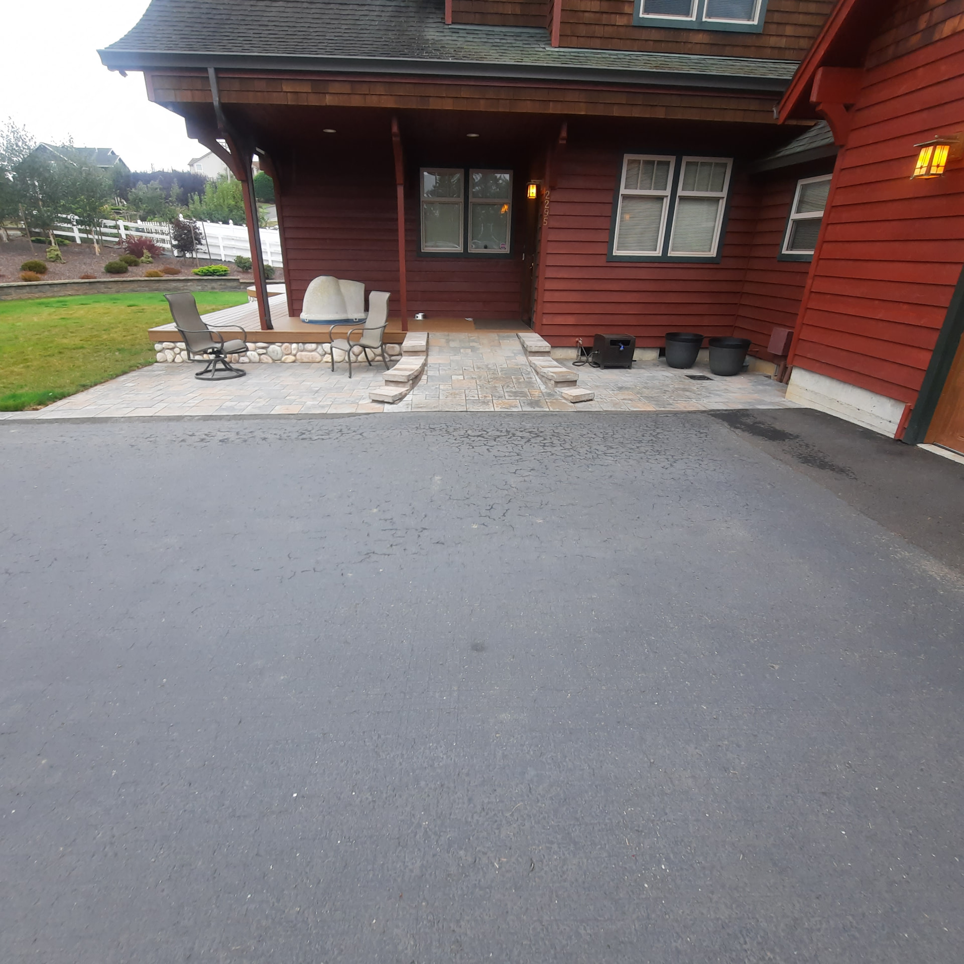 Paver entry landing and steps connecting the front door and deck to the asphalt driveway, with lawn and planted beds beyond