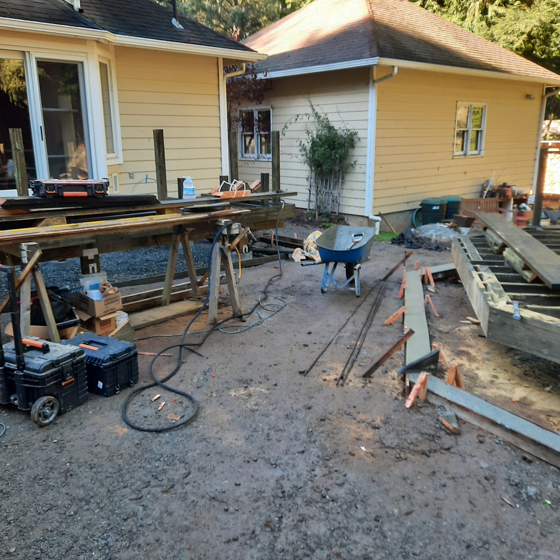 Deck framing underway with sawhorses, joists, posts, and tools staged across the work area