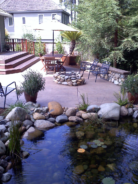 Pond, patio, deck, stone wall, seating, and planting integrated into one outdoor living space.