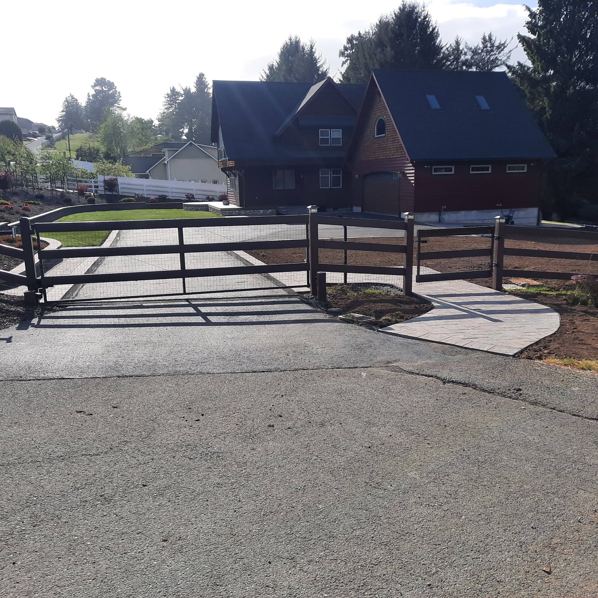 Automatic gate and dark rail fencing at the property entrance with a stamped concrete driveway and walkway leading to the house