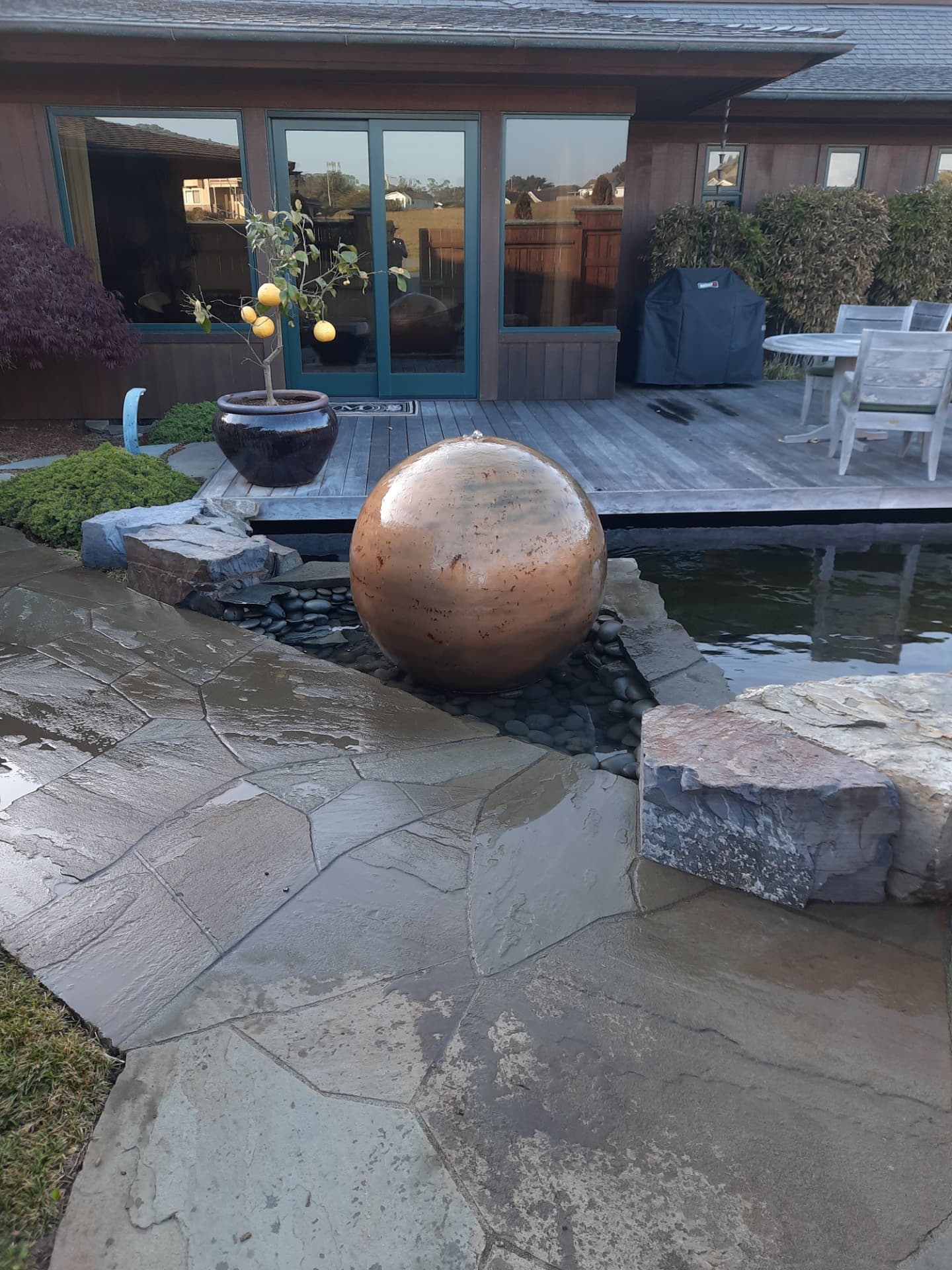 Copper sphere bubbler set in river cobble beside a flagstone patio and pond edge
