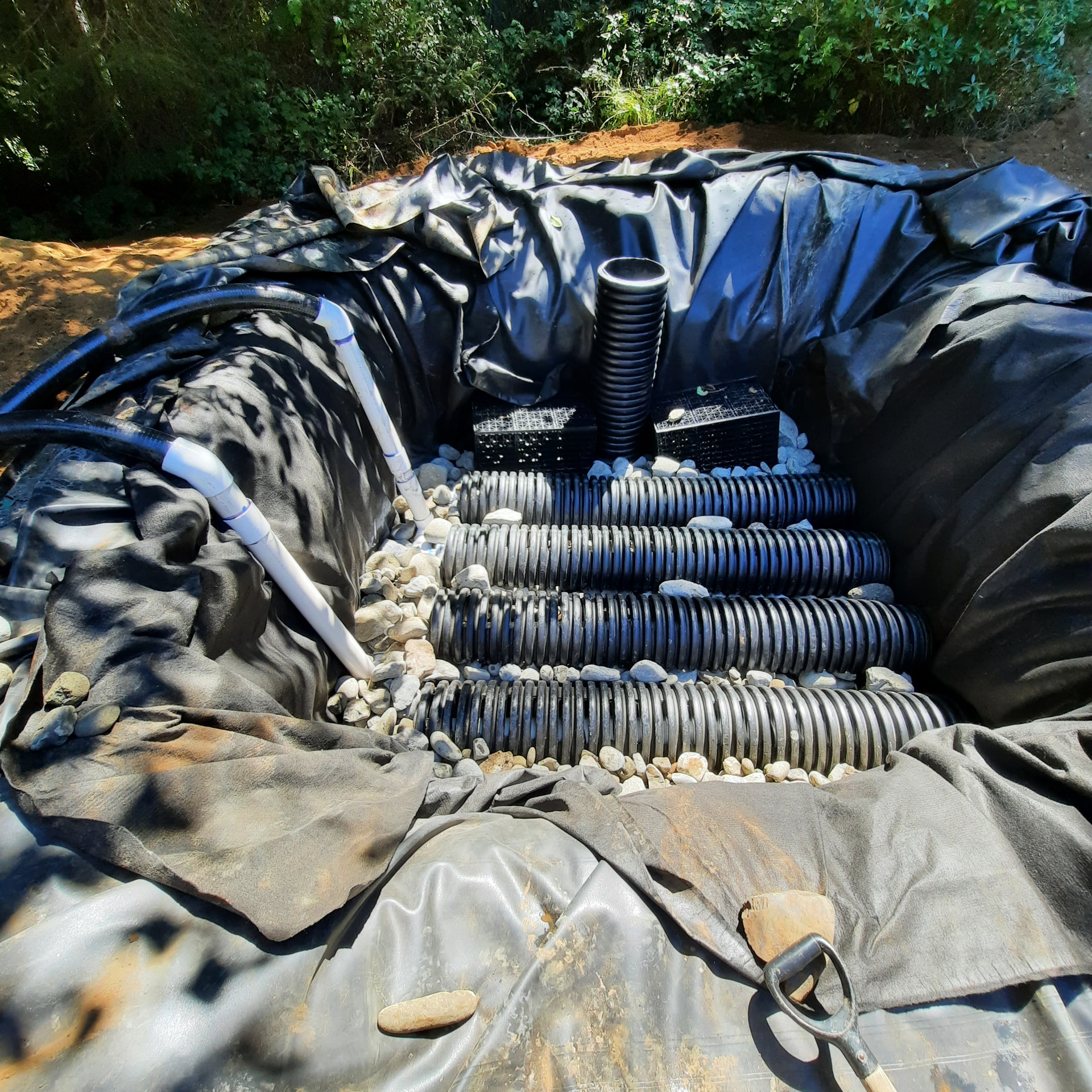 Filtration and circulation infrastructure under construction with liner, perforated pipe, and plumbing