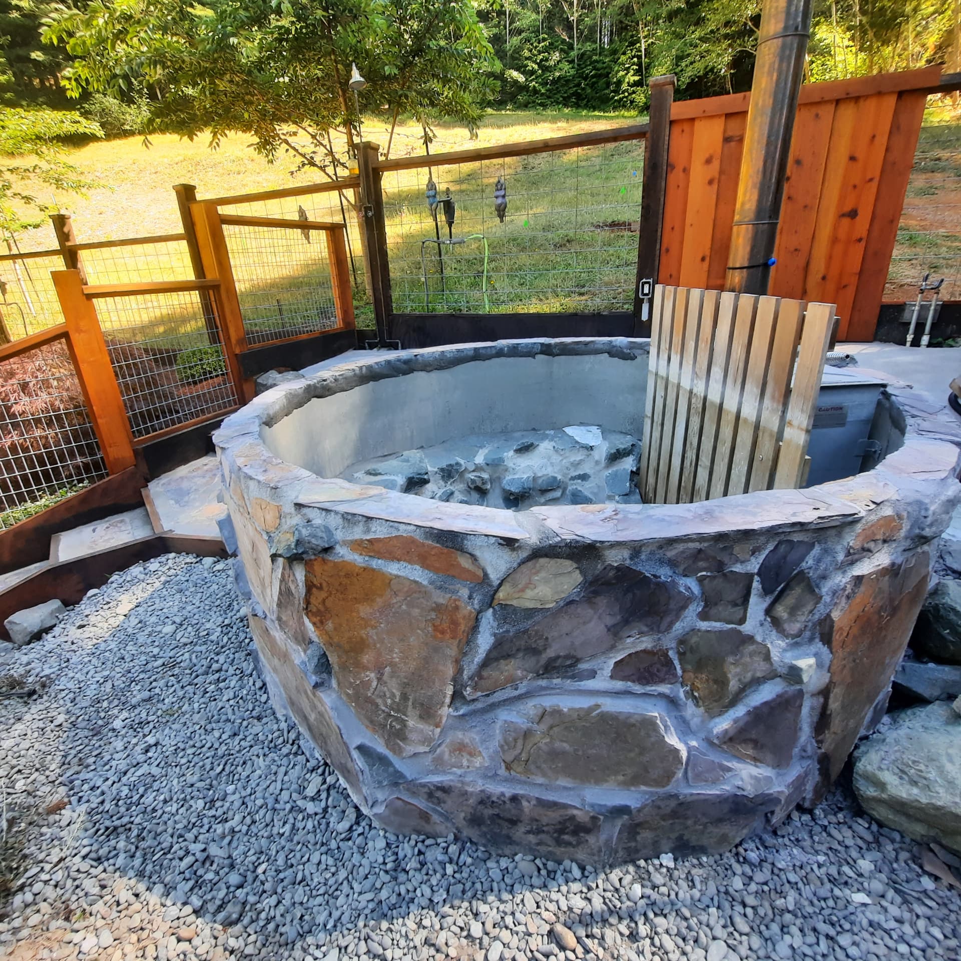 Wood-fired hot tub built from a concrete stock tank with stone facing and a chimney