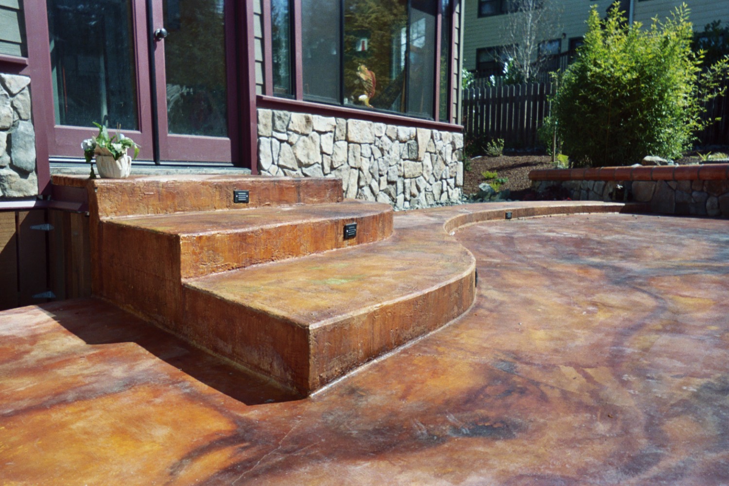 Curved decorative-concrete steps and patio with step lighting, stone veneer, and a capped wall.