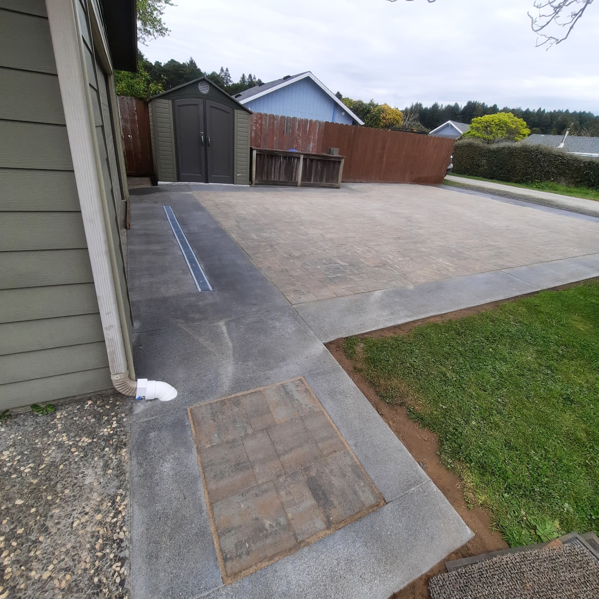 Finished paver driveway with a linear channel drain running along the house edge
