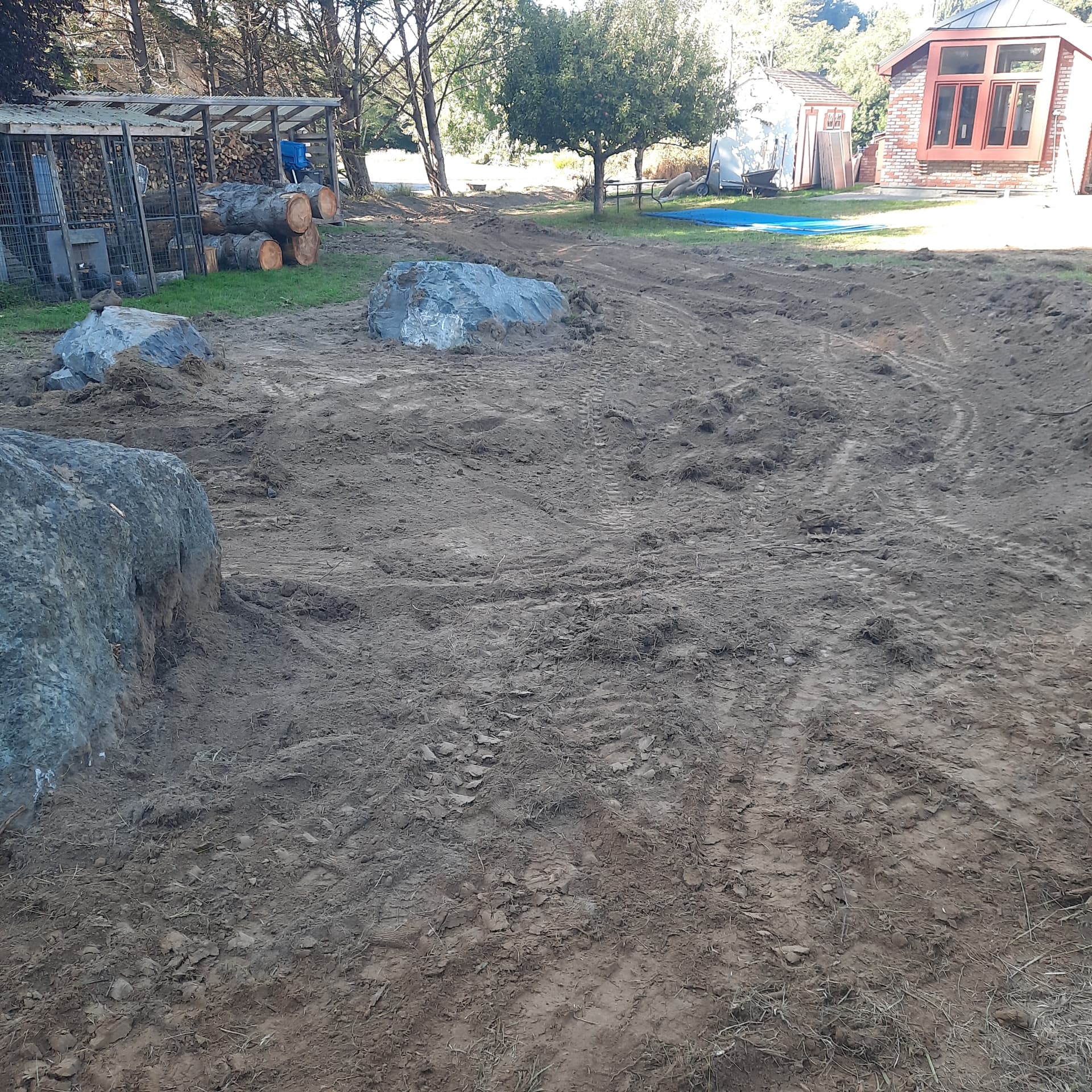 A cleared and rough-graded property at Jacoby Creek with one- and two-ton boulders set as part of a water management design, logs stacked for removal.