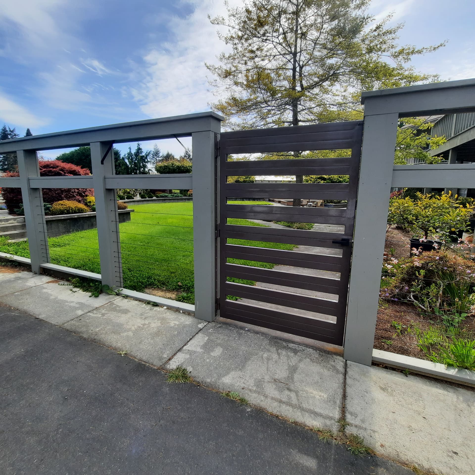 Rebuilt courtyard enclosure with steel cable infill and a custom steel gate open to the lawn