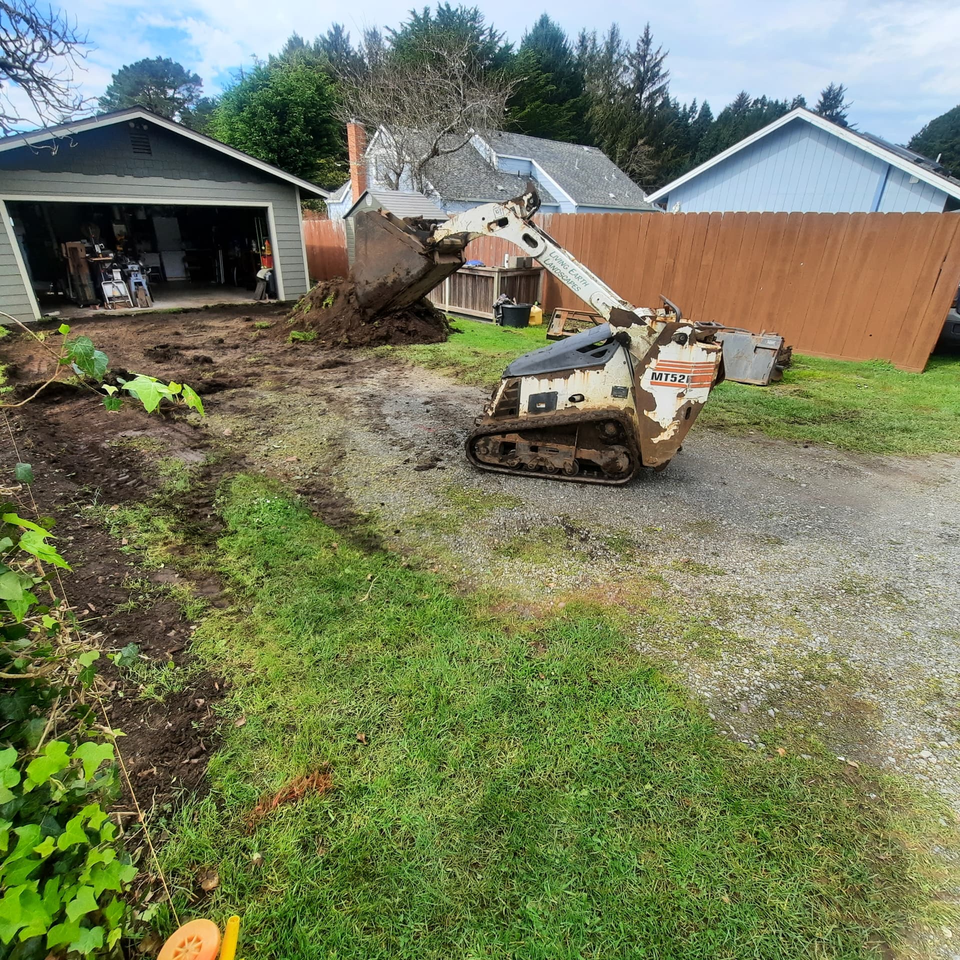 Existing gravel driveway being regraded by a compact track loader beside the garage
