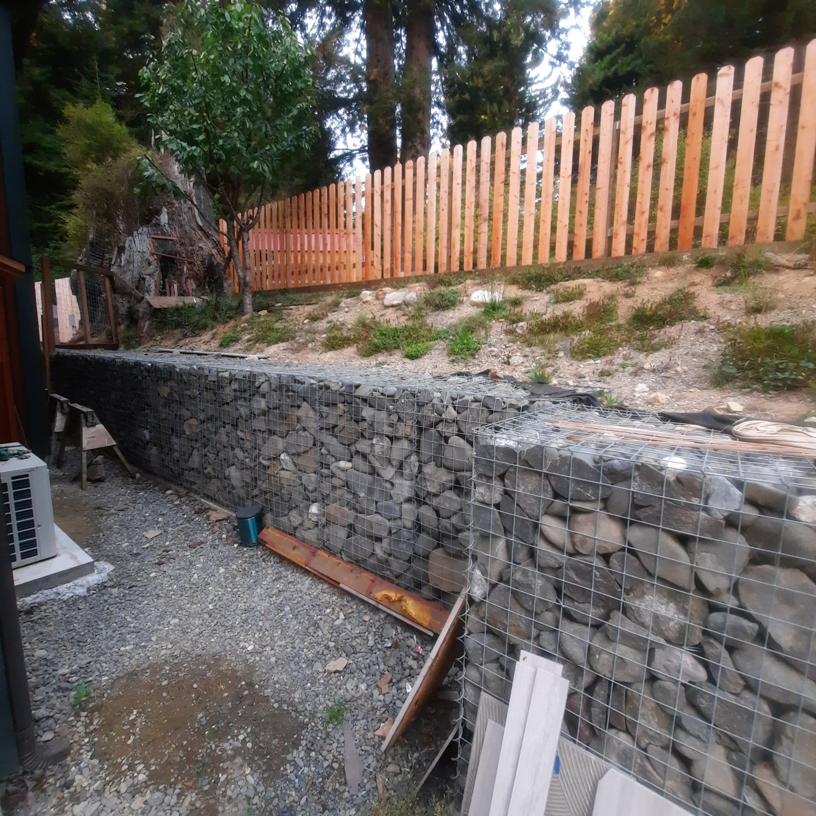 Photograph of a newly built stone-filled gabion wall below a bare slope and a wood picket fence.