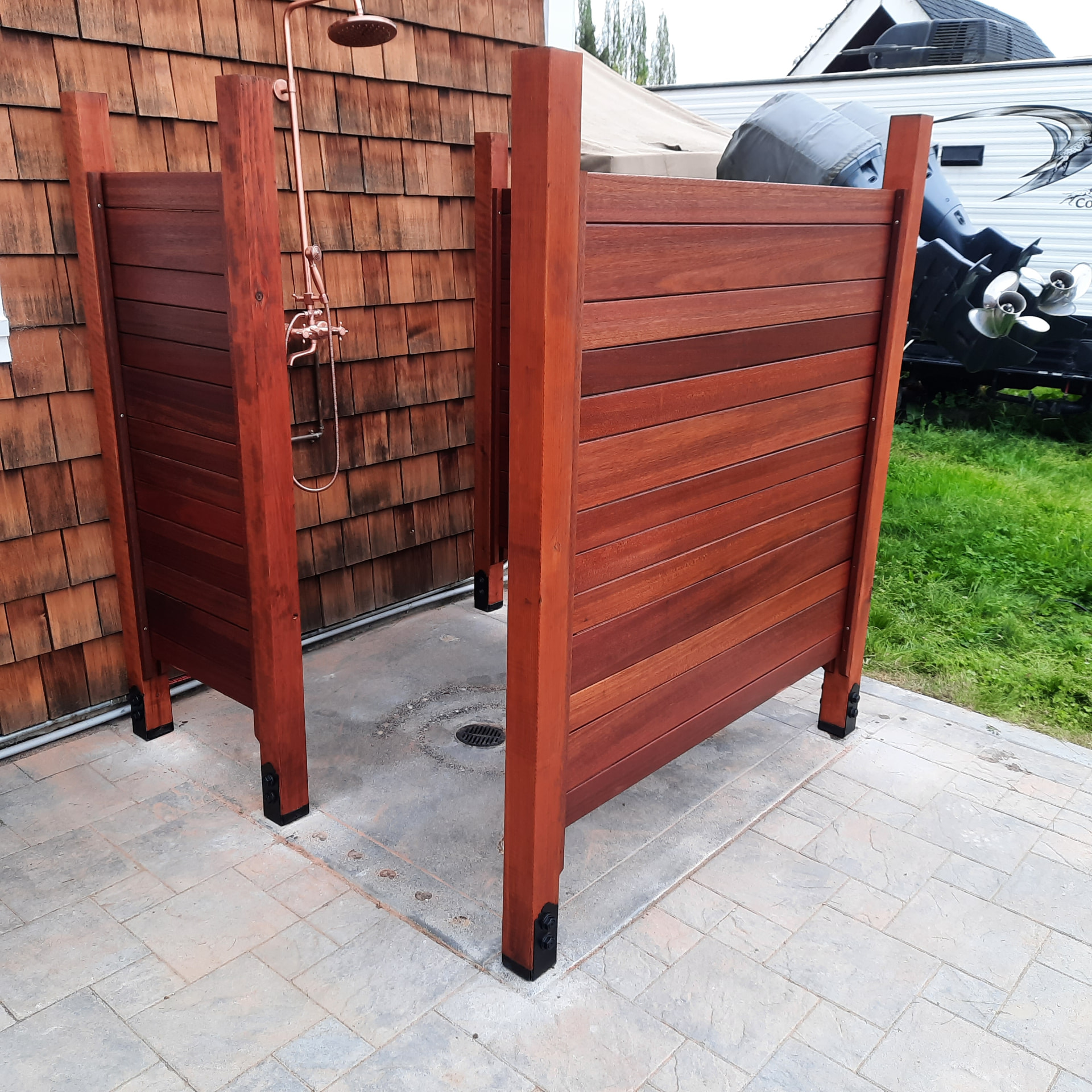 Hardwood outdoor shower enclosure with copper fixtures on a paver patio