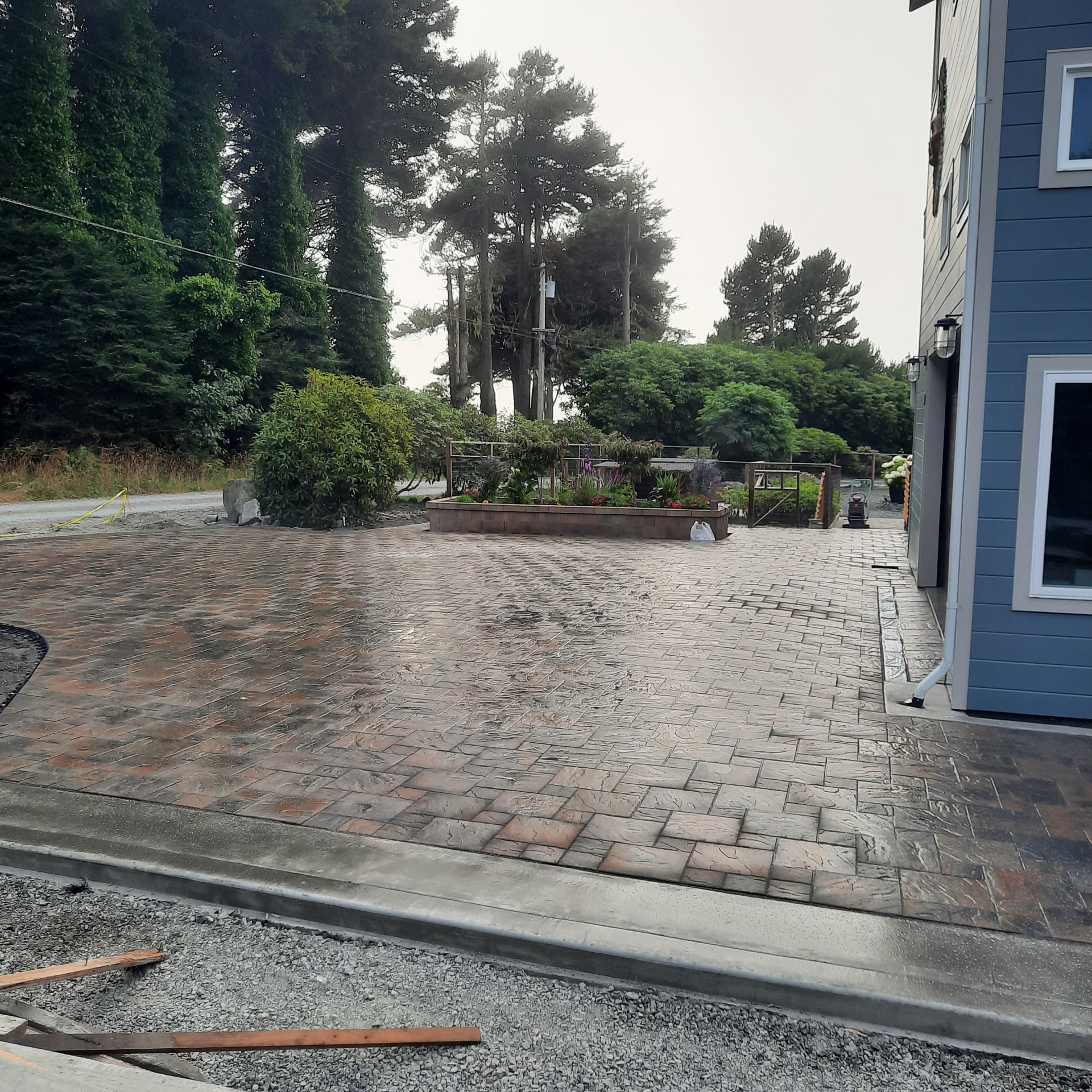Finished stamped paver driveway wrapping around a blue home with a raised planter bed alongside